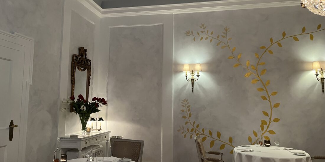 Elegantes Restaurant mit Wandmalerei, Kronleuchter und weiß gedeckten Tischen